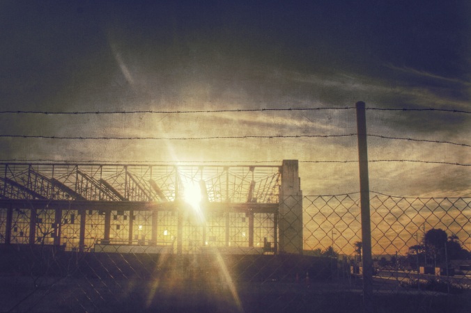 Steel skeleton of disused hangar, Hobsonville Point, Auckland. Shot at sunset with the sun behind the building. Image: Su Leslie, 2016. Edited with Snapseed and Stackables.