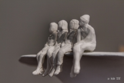"I have learned that to be with those I like is enough." Walt Whitman. Close up shot of four clay figures seated on bench. Detail from uture Islands exhibition, Tauranga Art Gallery, NZ. Image: Su Leslie, 2018