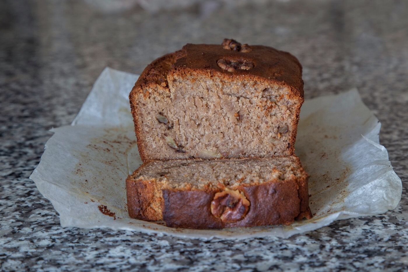 Close up colour shot of home-made sourdough banana bread resting on baking paper on kitchen bench.  Loaf has been cut, and one slice lies in front of lower part of the loaf. Image: Su Leslie 2019 